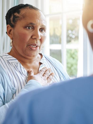 Senior heavy African American woman holding hand to chest speaking to health care worker
