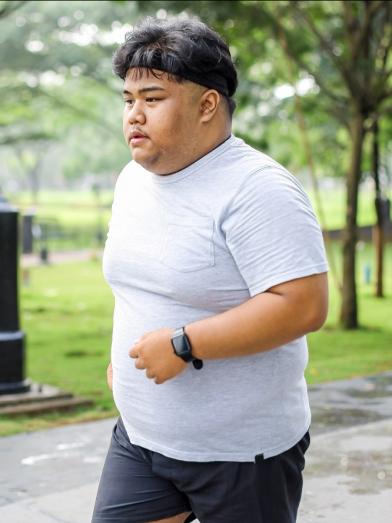 An overweight man jogging in a parl