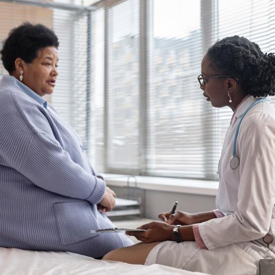Overweight African American senior woman talking to African American female physician in hospital room