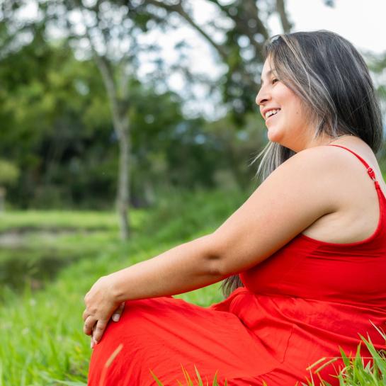 Latina woman in red dress sitting outside next to pond