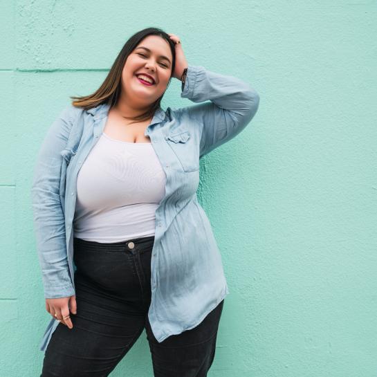 Smiling plus-size young woman standing in front of a concrete wall painted light green