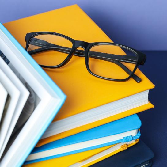 Black glasses sitting on top of stack of books