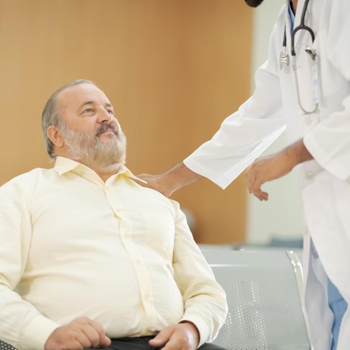Senior overweight man being spoken to by physician in waiting room