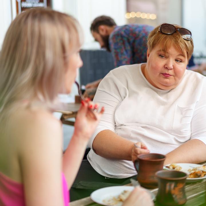 Overweight mother talking with daughter in cafe having lunch