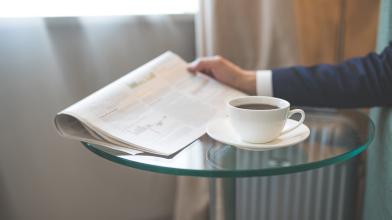 Business man reading newspaper on glasstop table with cup of coffee