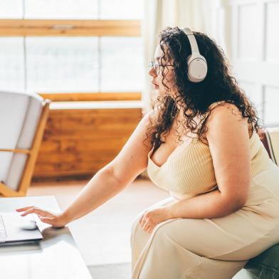 Overweight young woman with headphones on browsing on her laptop computer