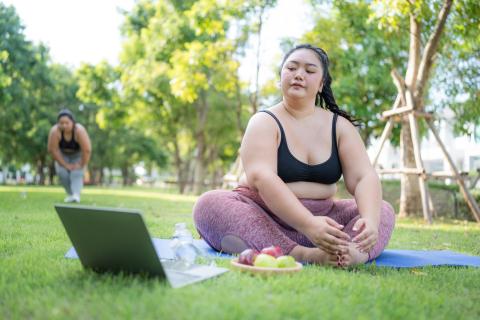 Overweight Asian woman in park looking at laptop while stretching
