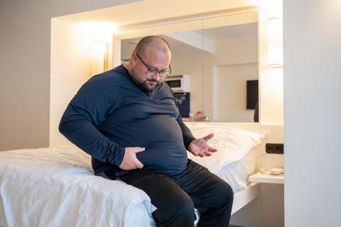 Overweight man on bed pinching the fat on his stomach