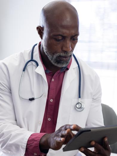 African American male doctor with stethoscope reading journal article on tablet